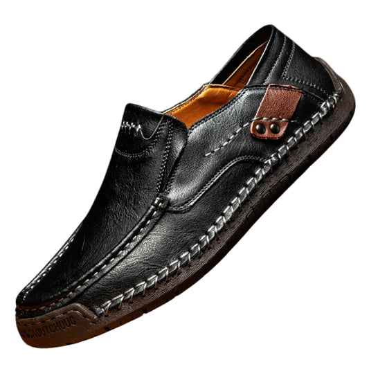 Black leather loafer shoe with brown stitching on a light gray background
