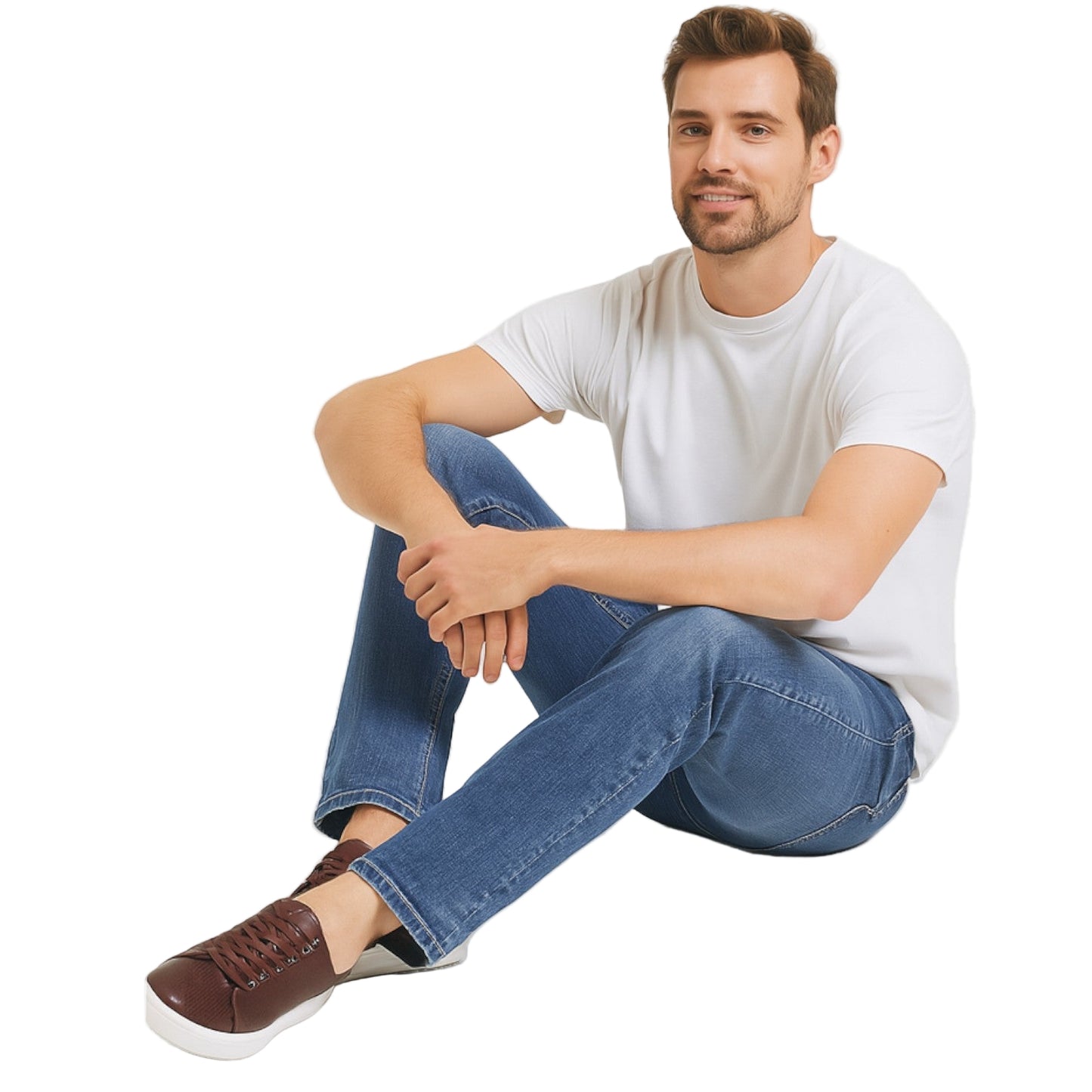 Man sitting on a white background wearing a white t-shirt, blue jeans, and brown shoes.